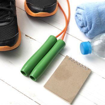 fitness equipment : running shoes,towel,jumping rope,water bottle and notepad on white wood table