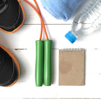 fitness equipment : running shoes,towel,jumping rope,water bottle and notepad on white wood table