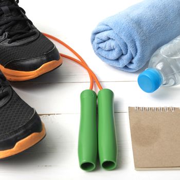 fitness equipment : running shoes,towel,jumping rope,water bottle and notepad on white wood table