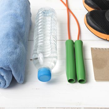 fitness equipment : running shoes,towel,jumping rope,water bottle and notepad on white wood table