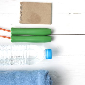 fitness equipment :towel,jumping rope,water bottle and notepad on white wood table