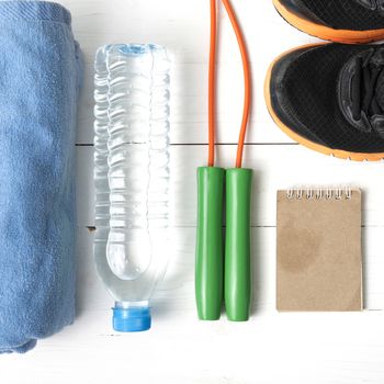 fitness equipment : running shoes,towel,jumping rope,water bottle and notepad on white wood table