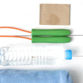 fitness equipment :towel,jumping rope,water bottle and notepad on white wood table