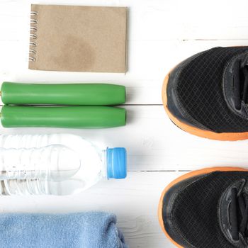 fitness equipment : running shoes,towel,jumping rope,water bottle and notepad on white wood table