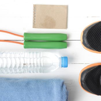fitness equipment : running shoes,towel,jumping rope,water bottle and notepad on white wood table