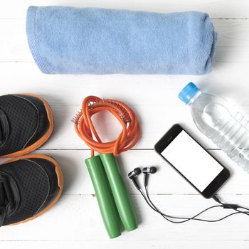 fitness equipment : running shoes,towel,jumping rope,water bottle and phone on white wood table