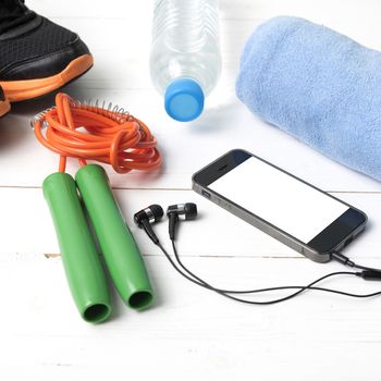 fitness equipment : running shoes,towel,jumping rope,water bottle and phone on white wood table