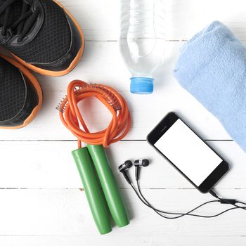 fitness equipment : running shoes,towel,jumping rope,water bottle and phone on white wood table