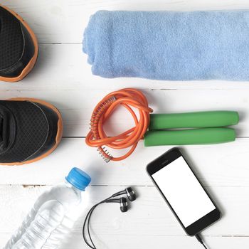 fitness equipment : running shoes,towel,jumping rope,water bottle and phone on white wood table