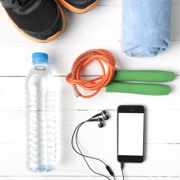 fitness equipment : running shoes,towel,jumping rope,water bottle and phone on white wood table