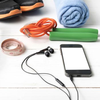 fitness equipment : running shoes,towel,jumping rope,phone and measuring tape on white wood table