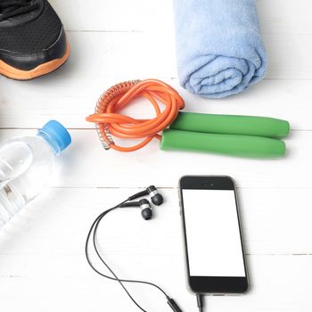 fitness equipment : running shoes,towel,jumping rope,water bottle and phone on white wood table