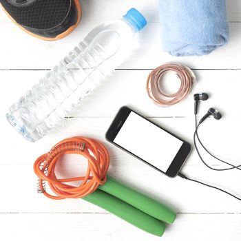 fitness equipment : running shoes,towel,jumping rope,water bottle,phone and measuring tape on white wood table