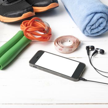 fitness equipment : running shoes,towel,jumping rope,water bottle,phone and measuring tape on white wood table