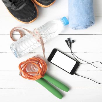 fitness equipment : running shoes,towel,jumping rope,water bottle,phone and measuring tape on white wood table