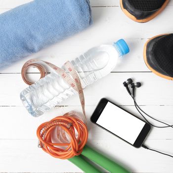 fitness equipment : running shoes,towel,jumping rope,water bottle,phone and measuring tape on white wood table