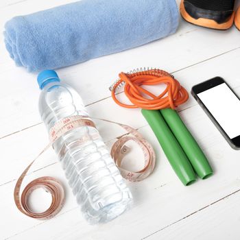 fitness equipment : running shoes,towel,jumping rope,water bottle,phone and measuring tape on white wood table