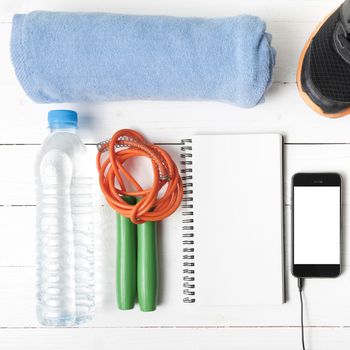fitness equipment : running shoes,towel,jumping rope,water bottle,phone and notepad on white wood table