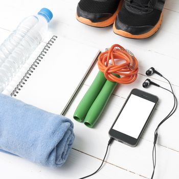 fitness equipment : running shoes,towel,jumping rope,water bottle,phone and notepad on white wood table