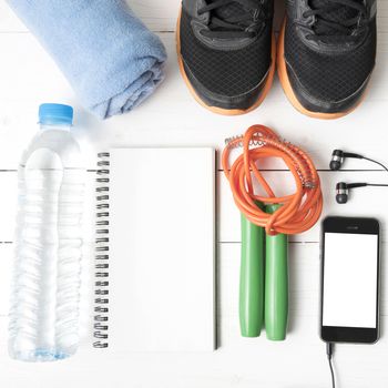 fitness equipment : running shoes,towel,jumping rope,water bottle,phone and notepad on white wood table