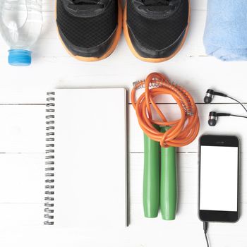 fitness equipment : running shoes,towel,jumping rope,water bottle,phone and notepad on white wood table