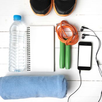 fitness equipment : running shoes,towel,jumping rope,water bottle,phone and notepad on white wood table