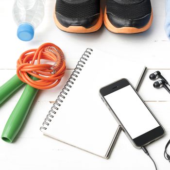 fitness equipment : running shoes,towel,jumping rope,water bottle,phone and notepad on white wood table