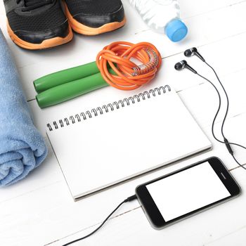 fitness equipment : running shoes,towel,jumping rope,water bottle,phone and notepad on white wood table