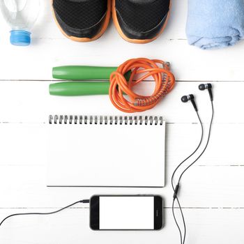 fitness equipment : running shoes,towel,jumping rope,water bottle,phone and notepad on white wood table