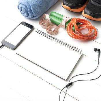 fitness equipment : running shoes,towel,jumping rope,phone,notepad and measuring tape on white wood table