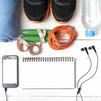 fitness equipment : running shoes,towel,jumping rope,water bottle,phone,notepad and measuring tape on white wood table