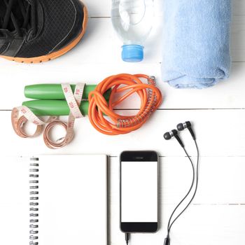 fitness equipment : running shoes,towel,jumping rope,water bottle,phone,notepad and measuring tape on white wood table