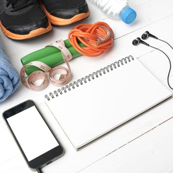 fitness equipment : running shoes,towel,jumping rope,water bottle,phone,notepad and measuring tape on white wood table