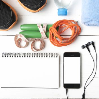 fitness equipment : running shoes,towel,jumping rope,water bottle,phone,notepad and measuring tape on white wood table