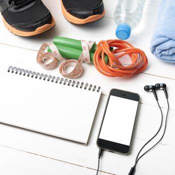 fitness equipment : running shoes,towel,jumping rope,water bottle,phone,notepad and measuring tape on white wood table