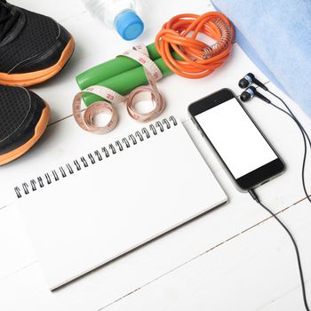 fitness equipment : running shoes,towel,jumping rope,water bottle,phone,notepad and measuring tape on white wood table