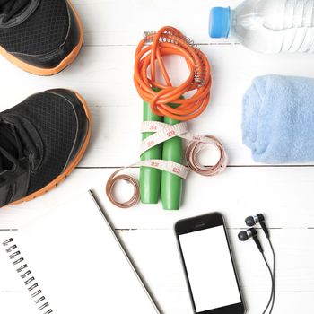 fitness equipment : running shoes,towel,jumping rope,water bottle,phone,notepad and measuring tape on white wood table