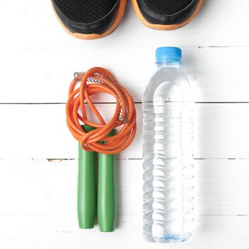 fitness equipment : running shoes,jumping rope and water bottle on white wood table