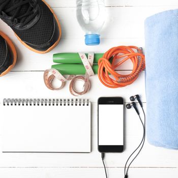 fitness equipment : running shoes,towel,jumping rope,water bottle,phone,notepad and measuring tape on white wood table