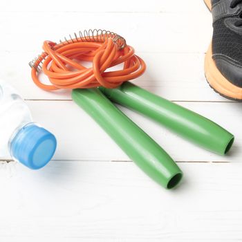 fitness equipment : running shoes,jumping rope and water bottle on white wood table