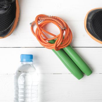 fitness equipment : running shoes,jumping rope and water bottle on white wood table