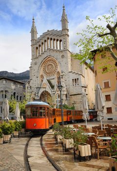 Old tram in the downtown of Soller in front of medieval gothic cathedral with huge rose window, Mallorca, Spain
