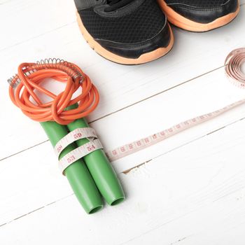 fitness equipment : running shoes,jumping rope and measuring tape on white wood table