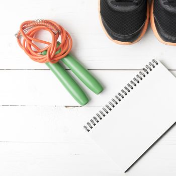 fitness equipment : running shoes,jumping rope and notepad on white wood table