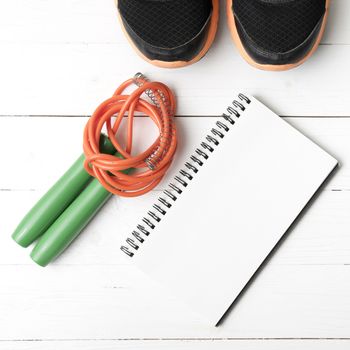 fitness equipment : running shoes,jumping rope and notepad on white wood table