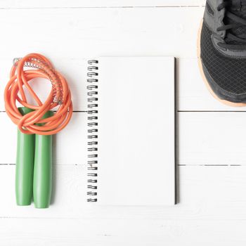 fitness equipment : running shoes,jumping rope and notepad on white wood table