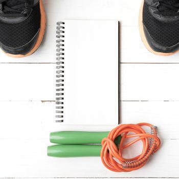 fitness equipment : running shoes,jumping rope and notepad on white wood table