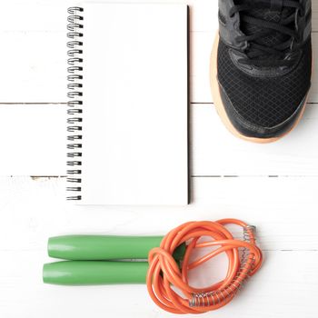 fitness equipment : running shoes,jumping rope and notepad on white wood table