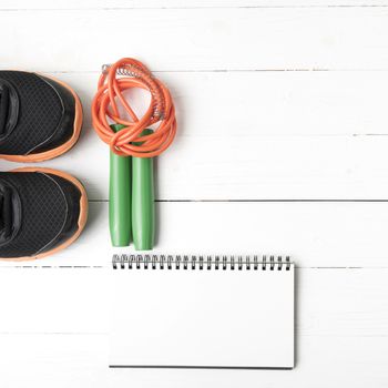 fitness equipment : running shoes,jumping rope and notepad on white wood table