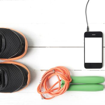 fitness equipment : running shoes,jumping rope and phone on white wood table